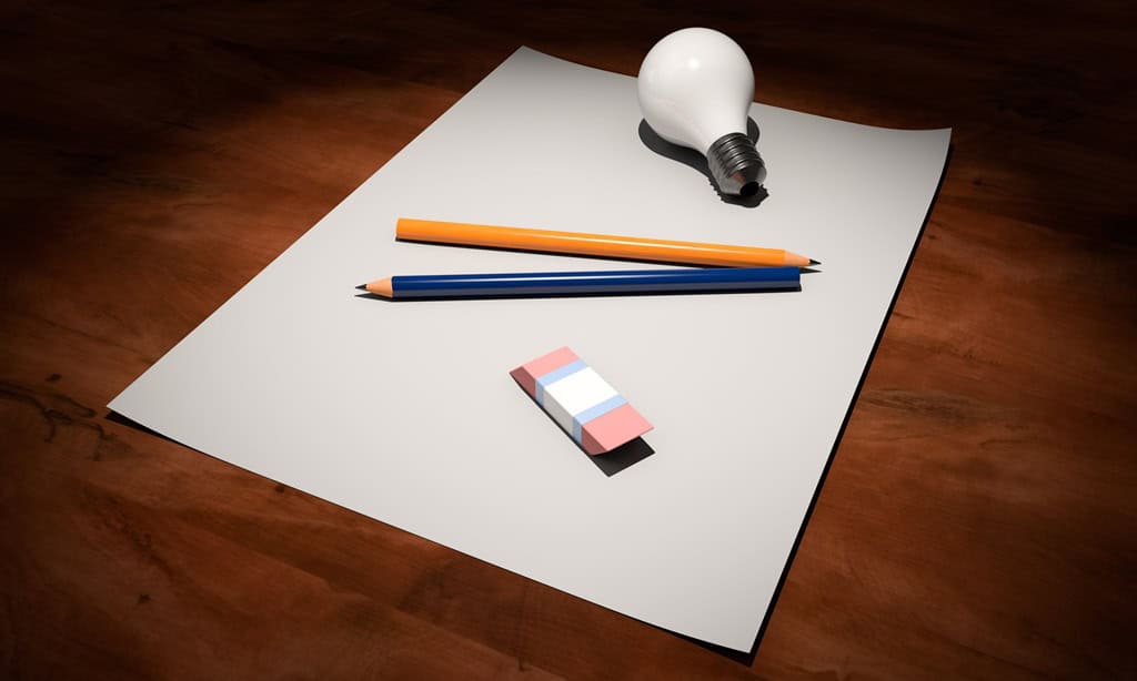 A lightbulb, coloured pencils, and an eraser resting on a sheet of paper